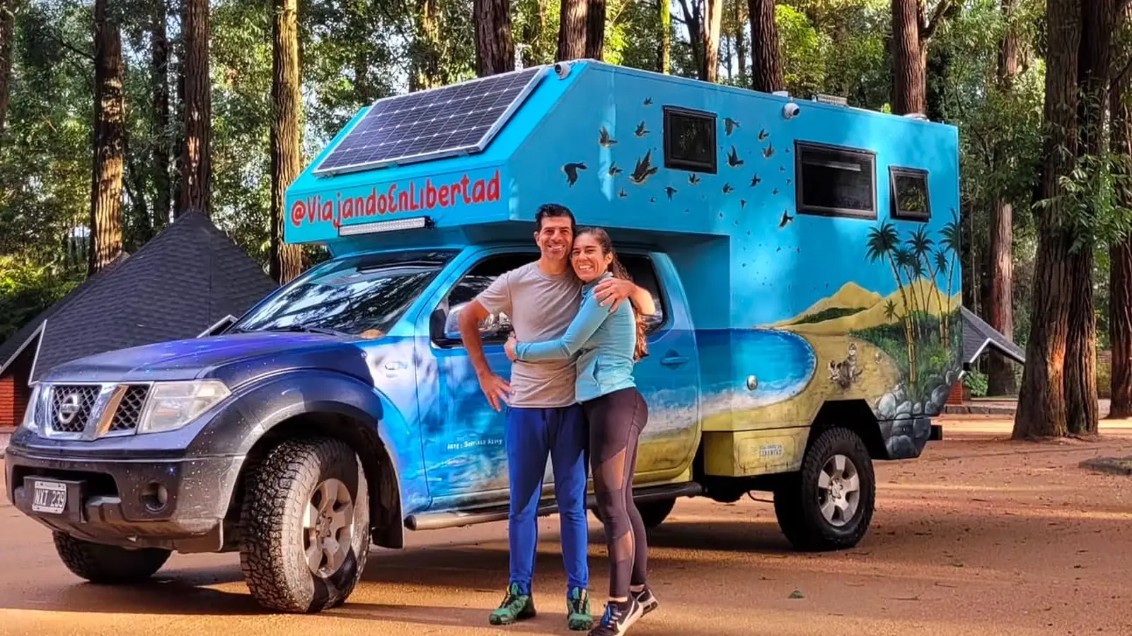 Tincho y Julie junto a la Frontineta, nuestro motorhome 4x4 pintado con paisajes y el nombre Viajando en Libertad